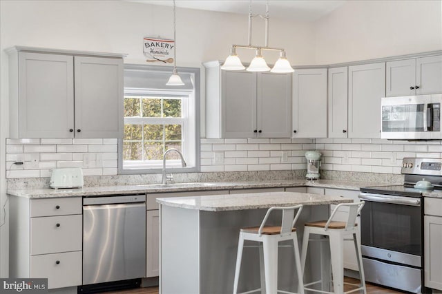 kitchen featuring appliances with stainless steel finishes, a sink, a center island, backsplash, and pendant lighting