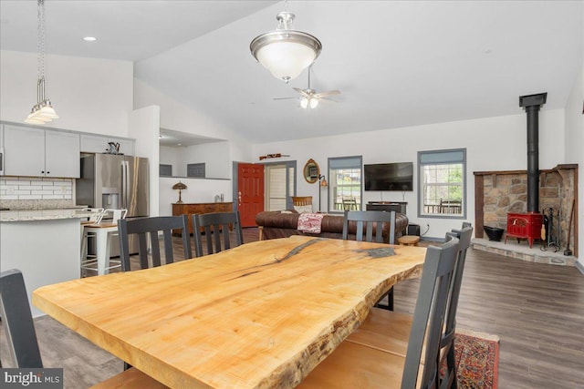 dining area with ceiling fan, vaulted ceiling, dark wood finished floors, and a wood stove