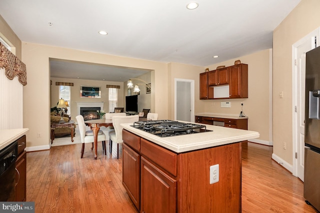 12216 Hillantrae Dr, Clinton, MD 20735 - kitchen with black appliances, a center island, light wood-style flooring, a lit fireplace, and light countertops