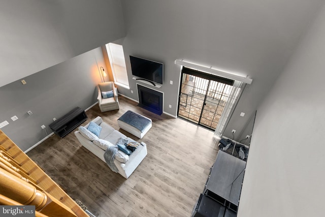 living room featuring wood finished floors, a fireplace with flush hearth, baseboards, and a high ceiling
