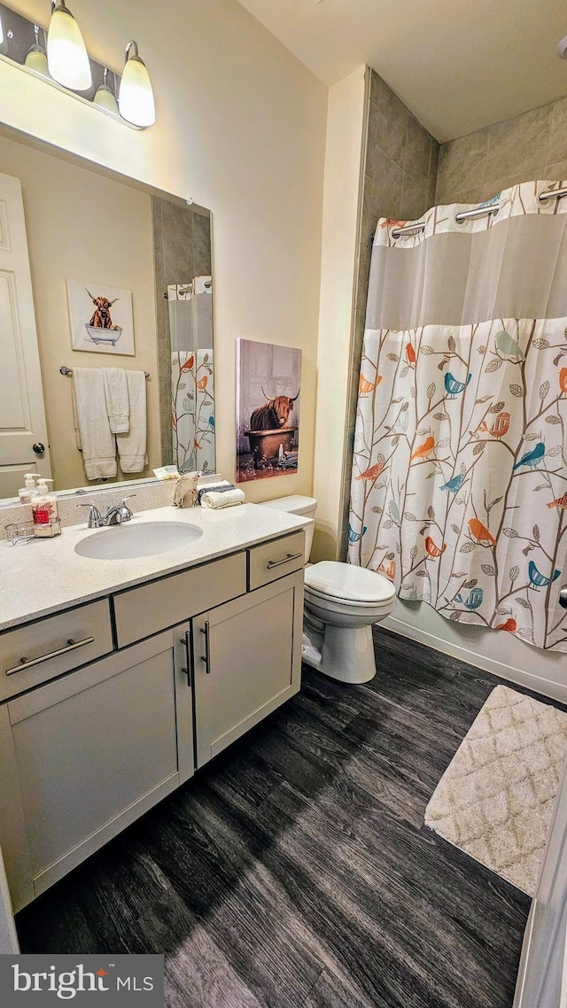 full bath featuring vanity, shower / tub combo with curtain, wood finished floors, and toilet