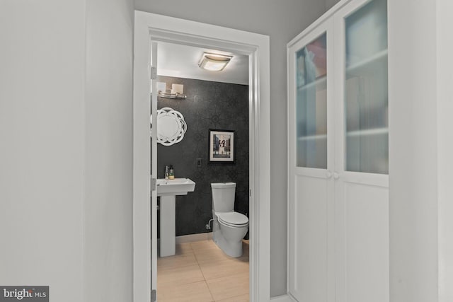 bathroom featuring toilet, wallpapered walls, baseboards, and an accent wall