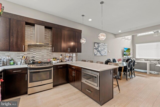 kitchen featuring light countertops, appliances with stainless steel finishes, a breakfast bar area, and wall chimney exhaust hood