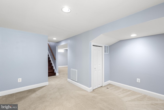 finished below grade area featuring light colored carpet, baseboards, visible vents, and stairway