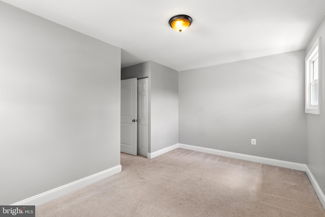 spare room with baseboards and light carpet