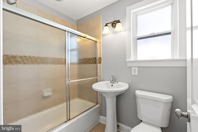 bathroom featuring a sink, toilet, and shower / bath combination with glass door