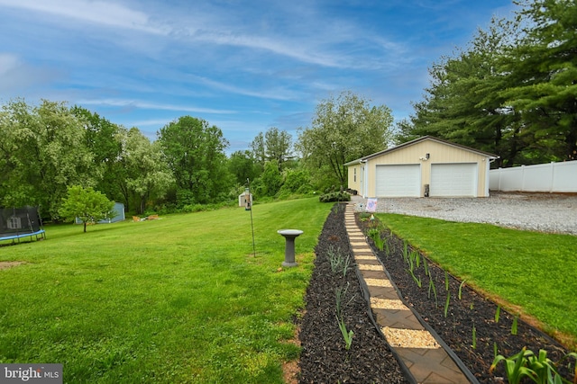 view of yard featuring a trampoline, an outdoor structure, fence, and a detached garage