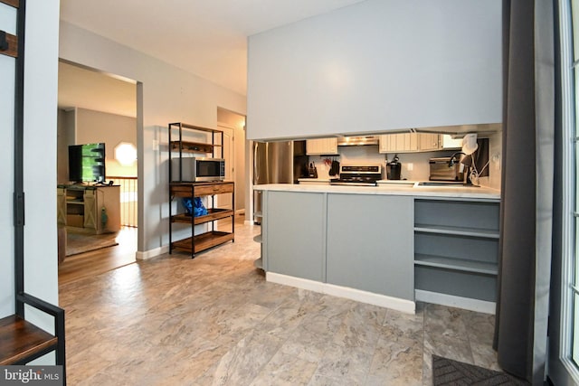 interior space with a sink, a peninsula, under cabinet range hood, light countertops, and appliances with stainless steel finishes