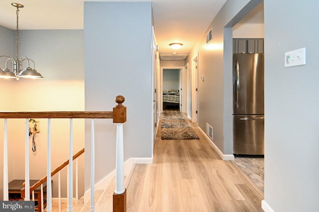 hallway with an inviting chandelier, baseboards, visible vents, and wood finished floors