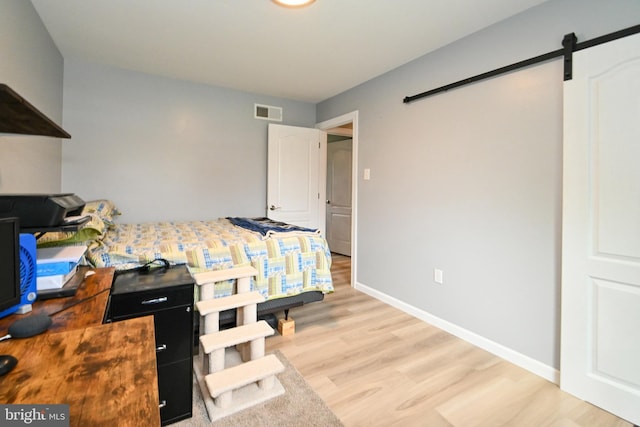 bedroom featuring baseboards, light wood-style floors, visible vents, and a barn door