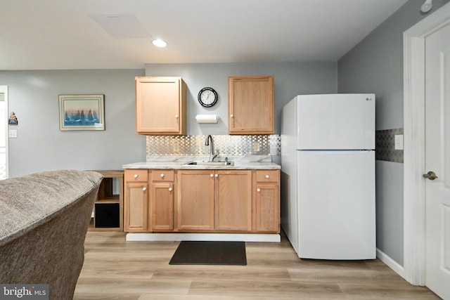 kitchen with freestanding refrigerator, light wood-style flooring, a sink, backsplash, and light countertops