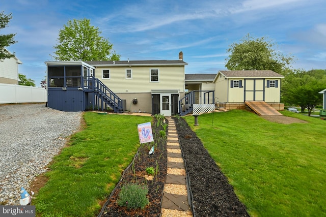 back of house with fence, stairs, an outdoor structure, a yard, and a sunroom