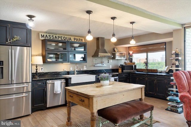 kitchen featuring a sink, stainless steel appliances, light wood-type flooring, a textured ceiling, and wall chimney range hood