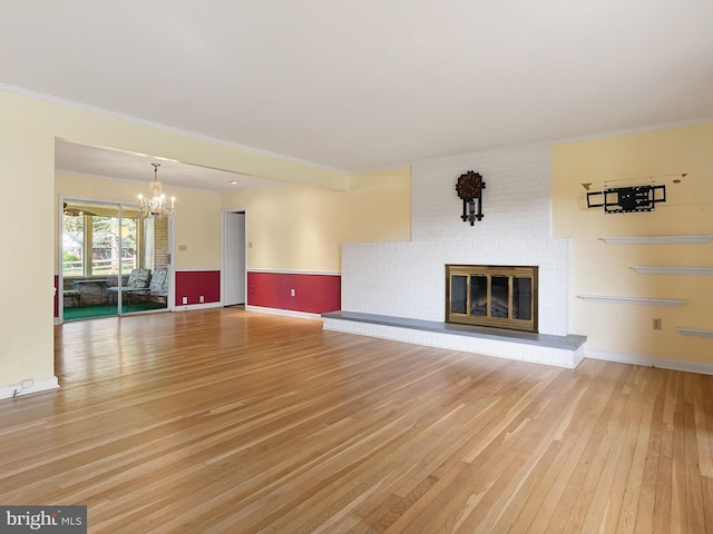 unfurnished living room with light wood-style floors, a chandelier, baseboards, and a brick fireplace