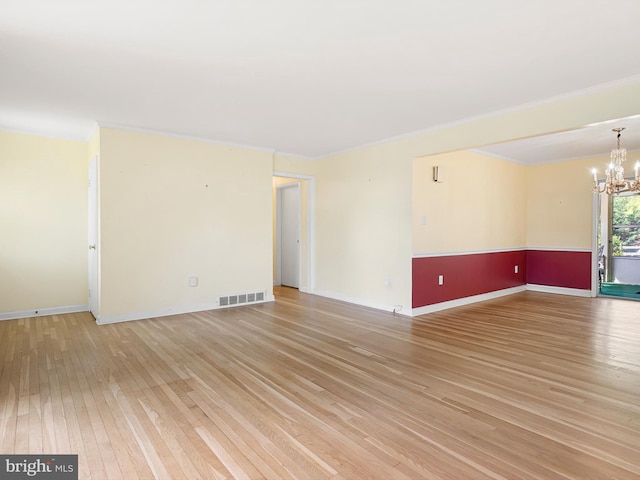 spare room featuring light wood finished floors, ornamental molding, visible vents, and an inviting chandelier