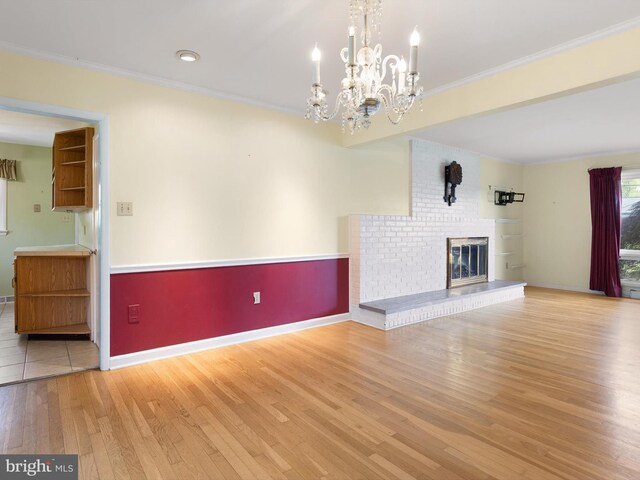 unfurnished living room with wood finished floors, a fireplace, crown molding, a chandelier, and baseboards