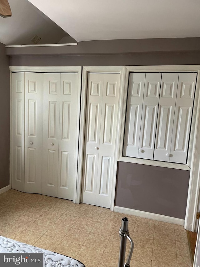 unfurnished bedroom with light tile patterned flooring, baseboards, and multiple closets