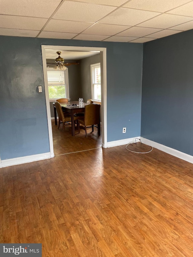 dining space with baseboards, a ceiling fan, a drop ceiling, and wood finished floors