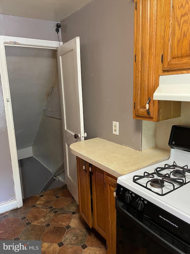 kitchen featuring brown cabinetry, light countertops, extractor fan, and range with gas cooktop