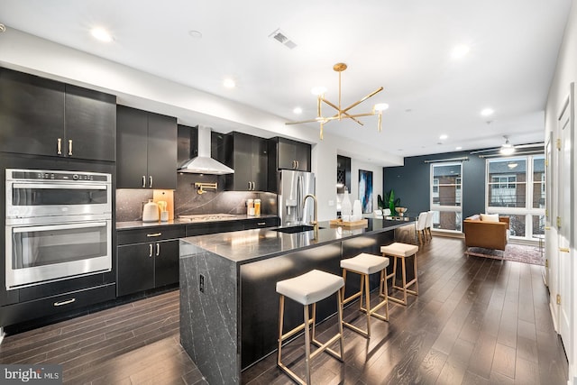 670 N 13th St, Philadelphia, PA 19123 - kitchen with wall chimney exhaust hood, dark cabinetry, appliances with stainless steel finishes, a sink, and a chandelier