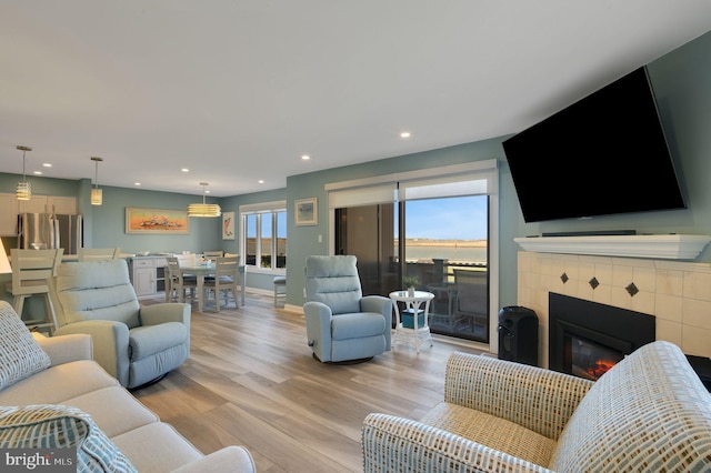 living room featuring light wood-style flooring, recessed lighting, a tiled fireplace, and baseboards