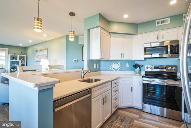 kitchen featuring appliances with stainless steel finishes, a sink, a peninsula, white cabinetry, and decorative light fixtures