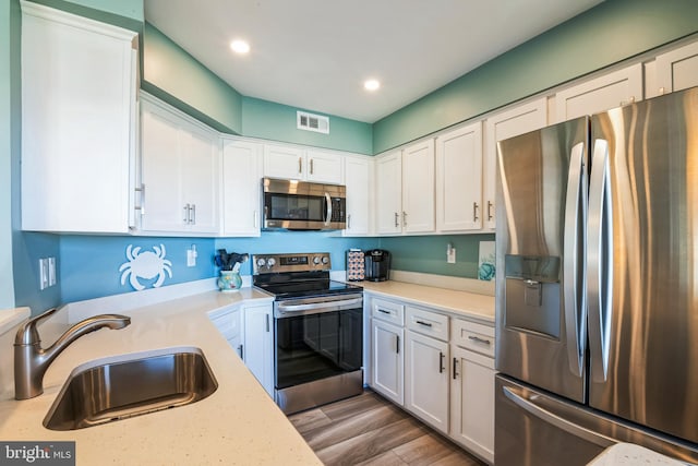 kitchen featuring appliances with stainless steel finishes, a sink, light countertops, white cabinetry, and recessed lighting