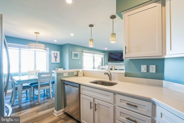 kitchen with appliances with stainless steel finishes, a sink, decorative light fixtures, light wood-style flooring, and white cabinetry