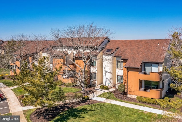 view of front of house with roof with shingles, a front lawn, and a balcony