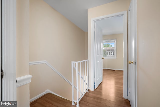 hallway with an upstairs landing, wood finished floors, and baseboards