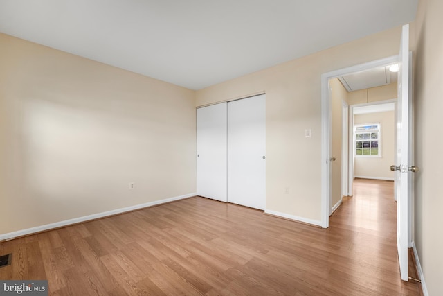 unfurnished bedroom with attic access, light wood-style flooring, baseboards, and a closet