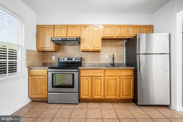 kitchen featuring appliances with stainless steel finishes, under cabinet range hood, a sink, tasteful backsplash, and light tile patterned floors