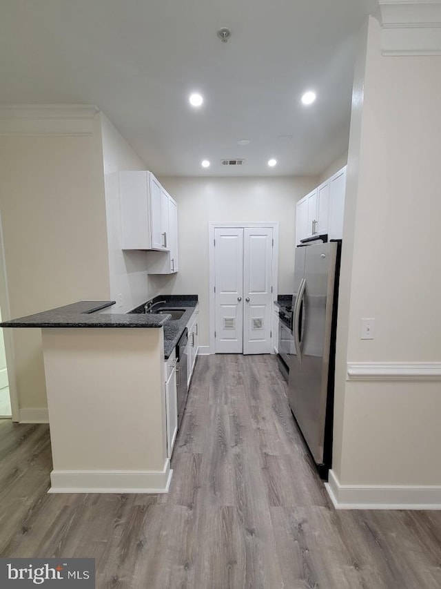 kitchen with light wood-type flooring, freestanding refrigerator, white cabinetry, and dark stone countertops