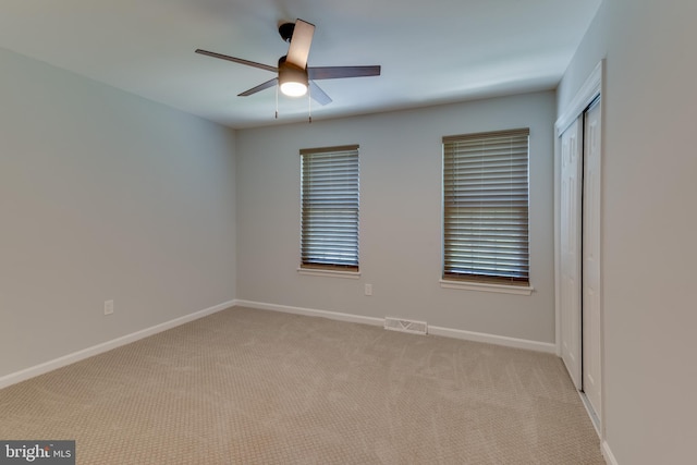 empty room featuring light colored carpet, a ceiling fan, and baseboards
