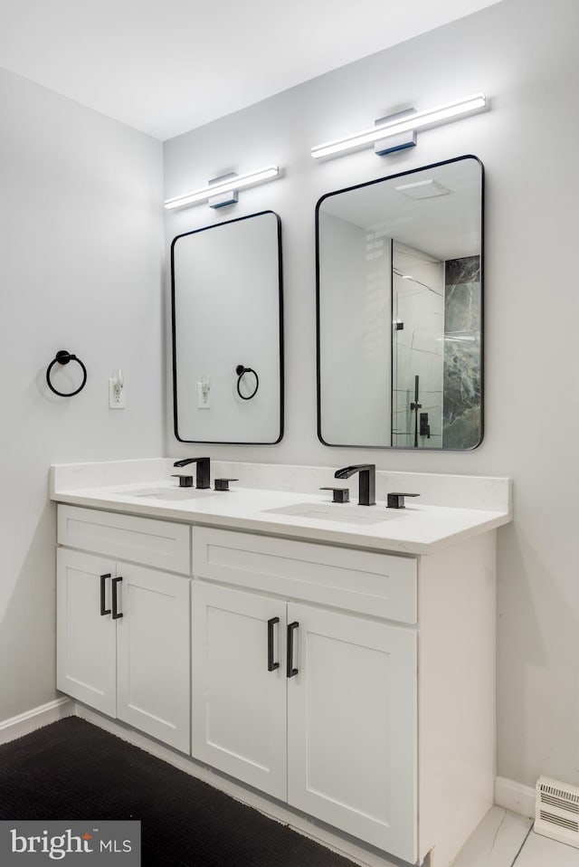 full bathroom with baseboards, double vanity, a shower with door, and a baseboard radiator