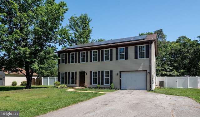 colonial-style house with roof mounted solar panels, driveway, an attached garage, and a gate