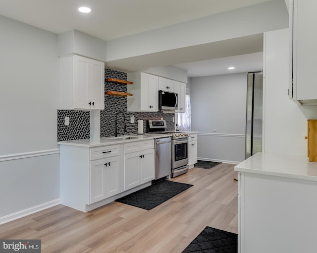 kitchen with a sink, appliances with stainless steel finishes, open shelves, white cabinetry, and tasteful backsplash