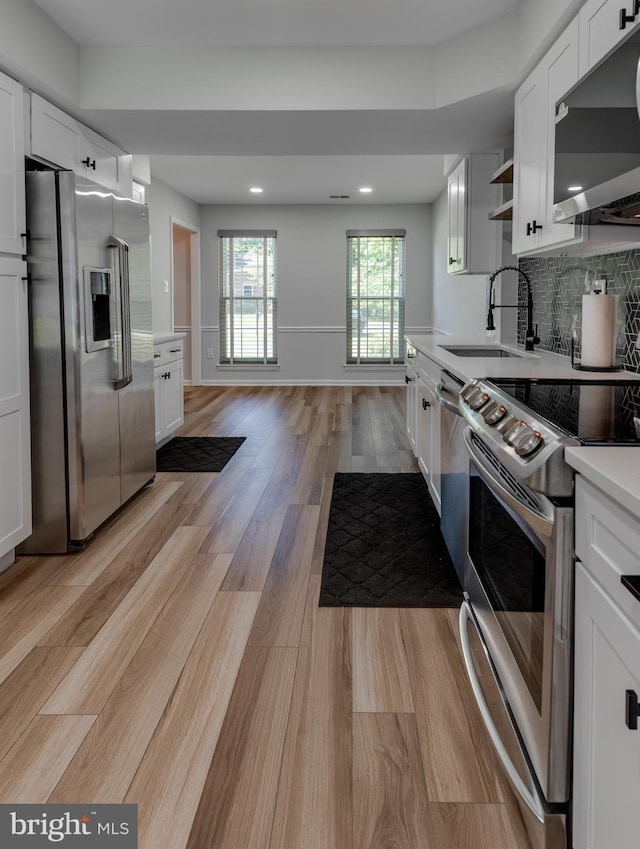 kitchen with appliances with stainless steel finishes, a sink, light countertops, white cabinetry, and recessed lighting