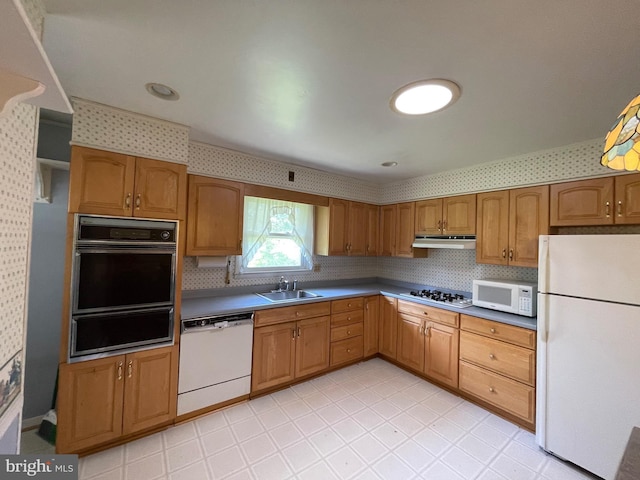 kitchen with brown cabinetry, white appliances, under cabinet range hood, a sink, and a warming drawer