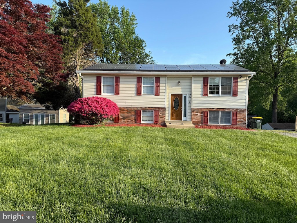 split foyer home with entry steps, a front lawn, and roof mounted solar panels