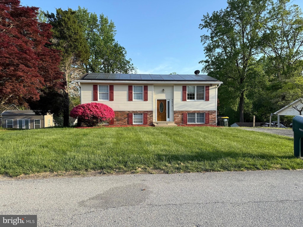 split foyer home with entry steps, brick siding, solar panels, and a front yard