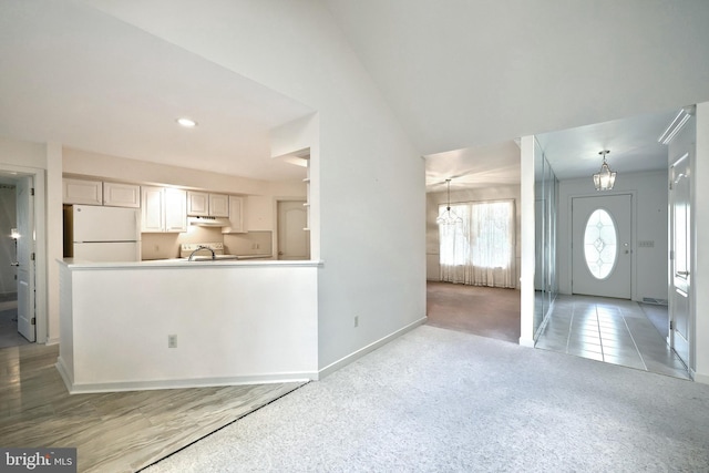 unfurnished living room featuring a sink, baseboards, light colored carpet, and a notable chandelier