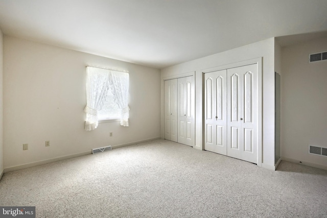 unfurnished bedroom with two closets, visible vents, and carpet
