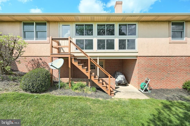 rear view of property featuring a chimney, a yard, stucco siding, and brick siding