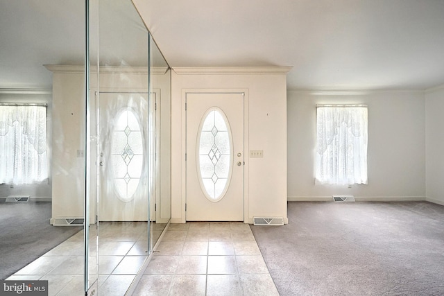 carpeted foyer entrance featuring crown molding, a wealth of natural light, and visible vents