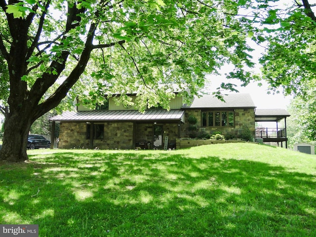 back of house with a yard, stone siding, a standing seam roof, and metal roof