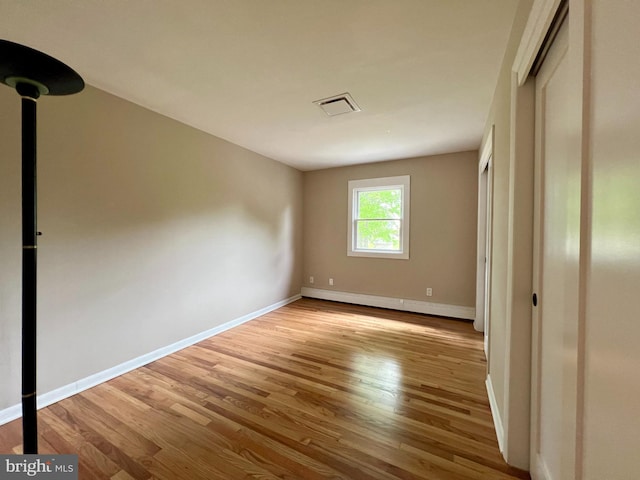 unfurnished bedroom with wood finished floors, a closet, visible vents, baseboards, and a baseboard heating unit