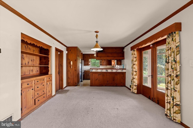 kitchen featuring crown molding, a peninsula, light carpet, brown cabinets, and hanging light fixtures
