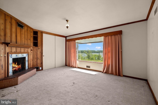 unfurnished living room featuring crown molding, carpet floors, a warm lit fireplace, and baseboards