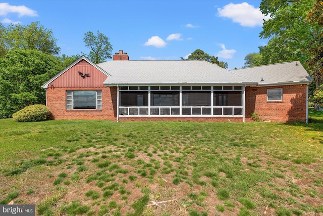 rear view of house featuring a sunroom, a lawn, a chimney, and brick siding